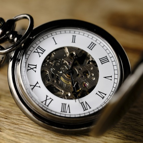 Close up photograph of a vintage pocket watch with roman numerals on the watch face.