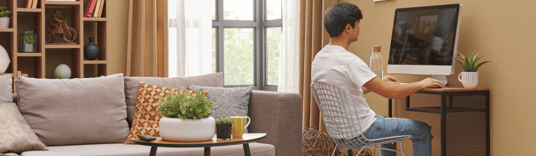 Comfortable home office setup with a young woman working on a desktop computer in a cozy living room environment.