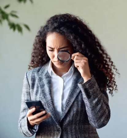 A business woman squints at her cell phone through a magnifying glass.