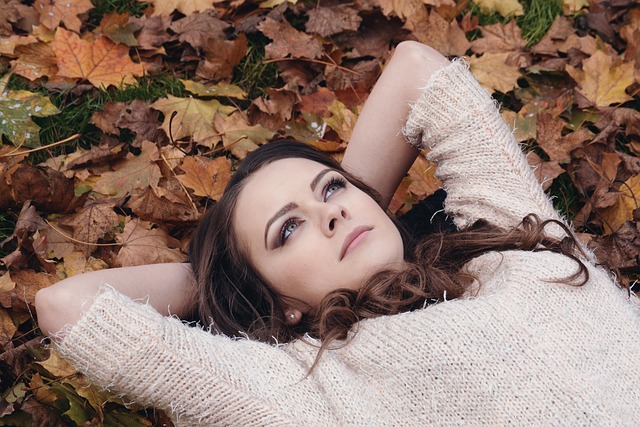 A woman lays in nature on the ground, her hands behind her head, looking at the sky and daydreaming