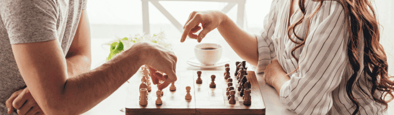 Close-up of two people playing chess at a wooden table in a bright, modern office environment.