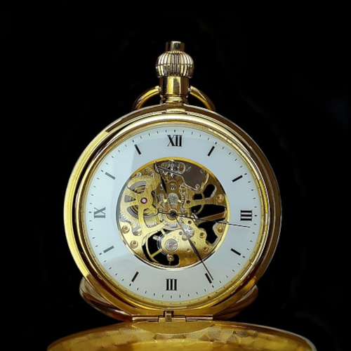A vintage gold pocket watch with roman numerals on the watch face. A decorative image is in the center.
