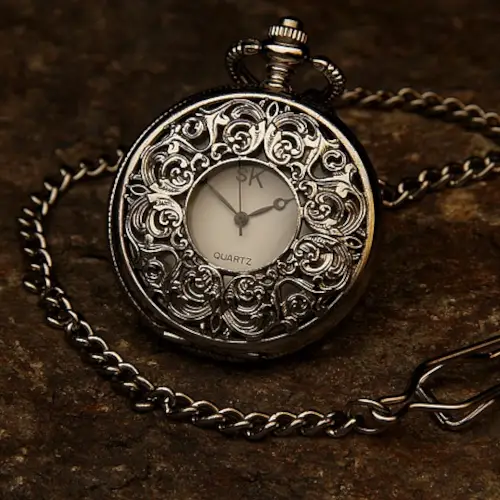 A ladies vintage pocket watch with a small watch face visible from a small window in the highly decorated, closed lid.
